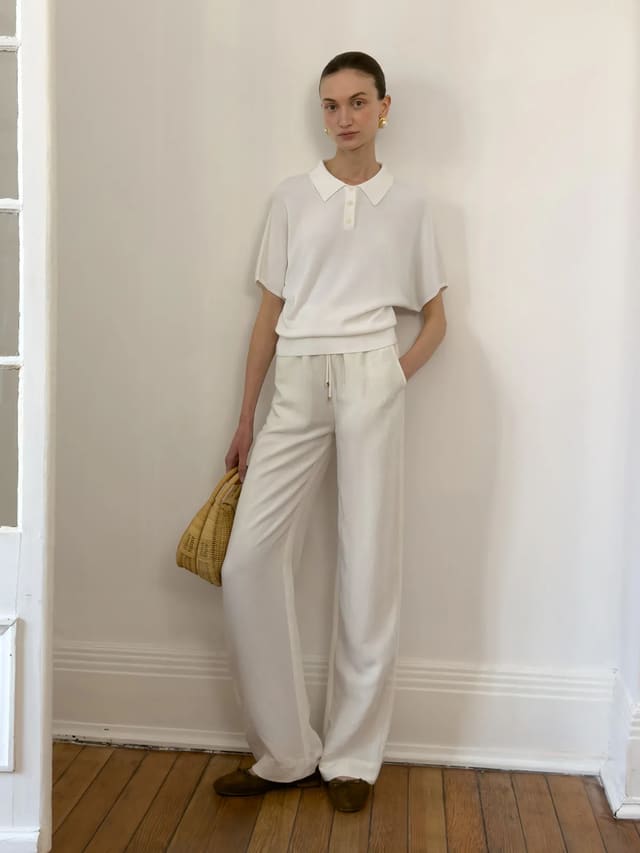 Model wearing white linen wide-leg trousers with white polo shirt and woven bag, Parisian chic styling