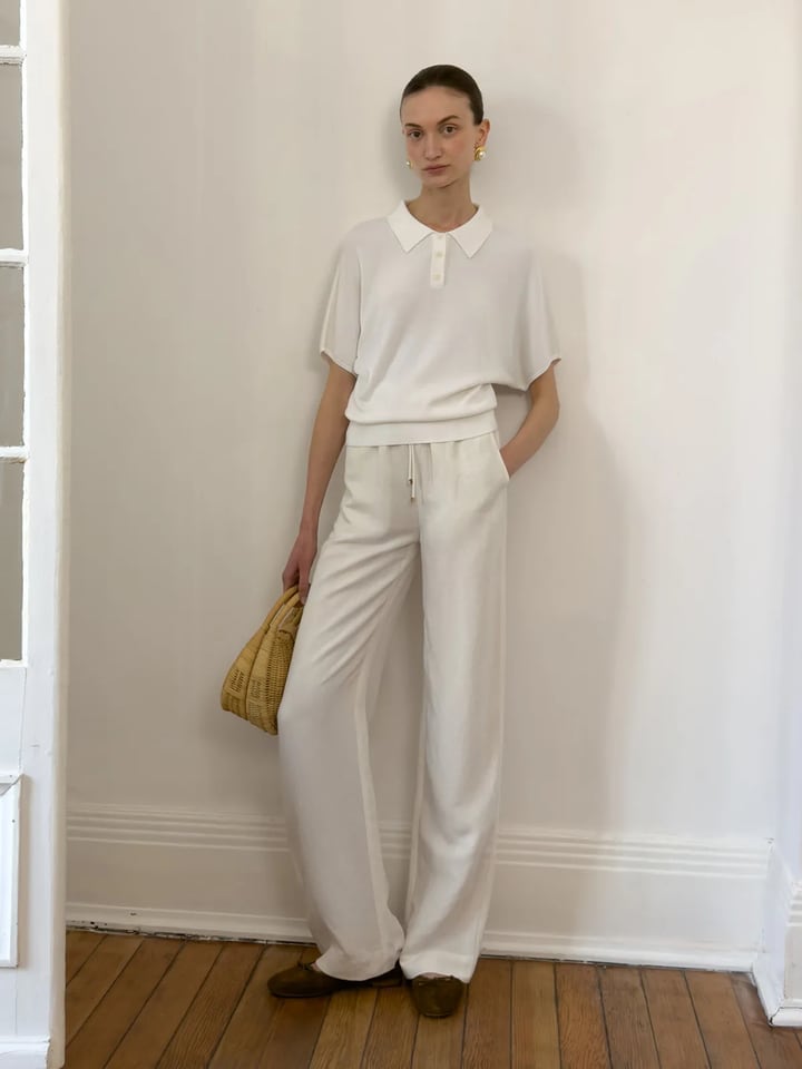 Model wearing white linen wide-leg trousers with white polo shirt and woven bag, Parisian chic styling