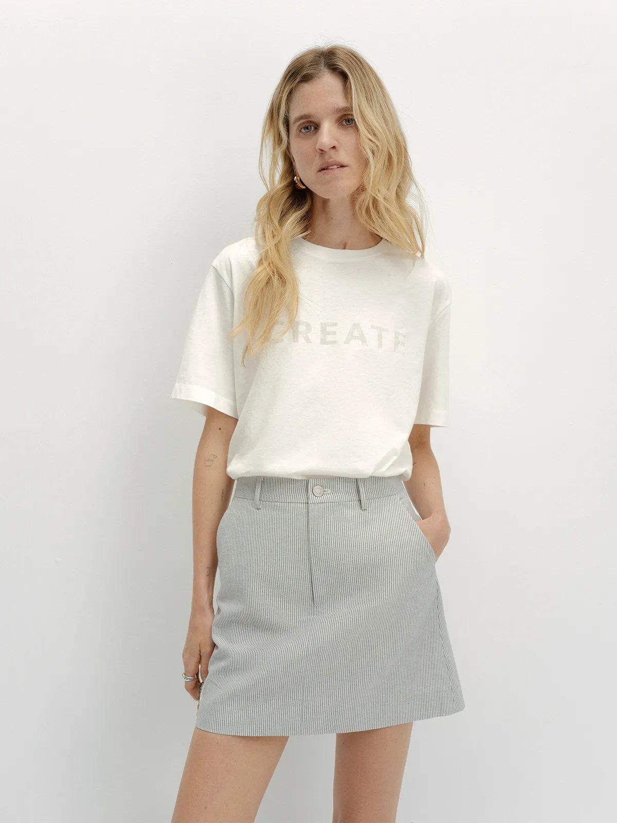 Front full-body look: DEVON Mini Skirt with 'CREATE' graphic tee and gold hoop earrings