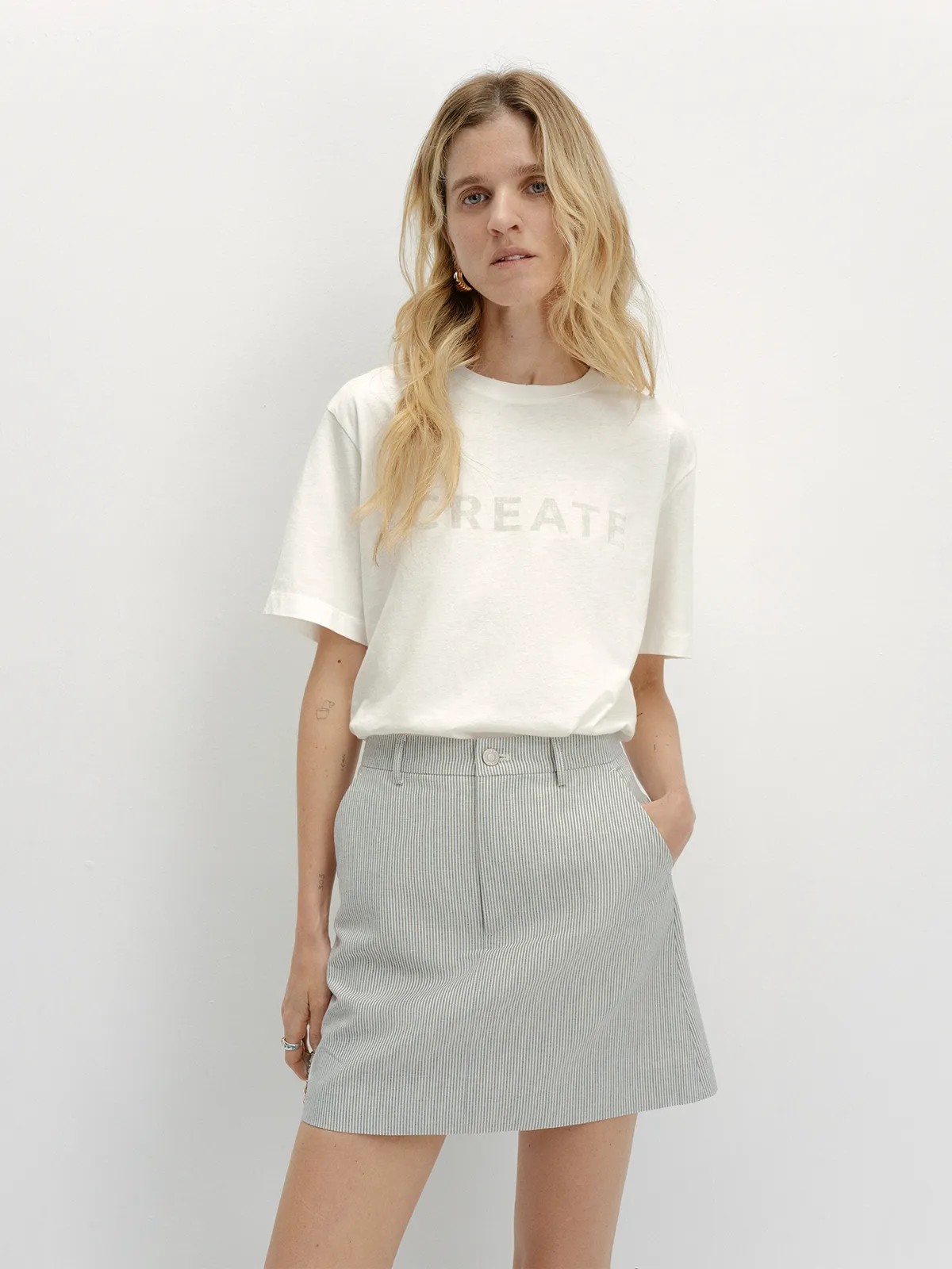 Front full-body look: DEVON Mini Skirt with 'CREATE' graphic tee and gold hoop earrings