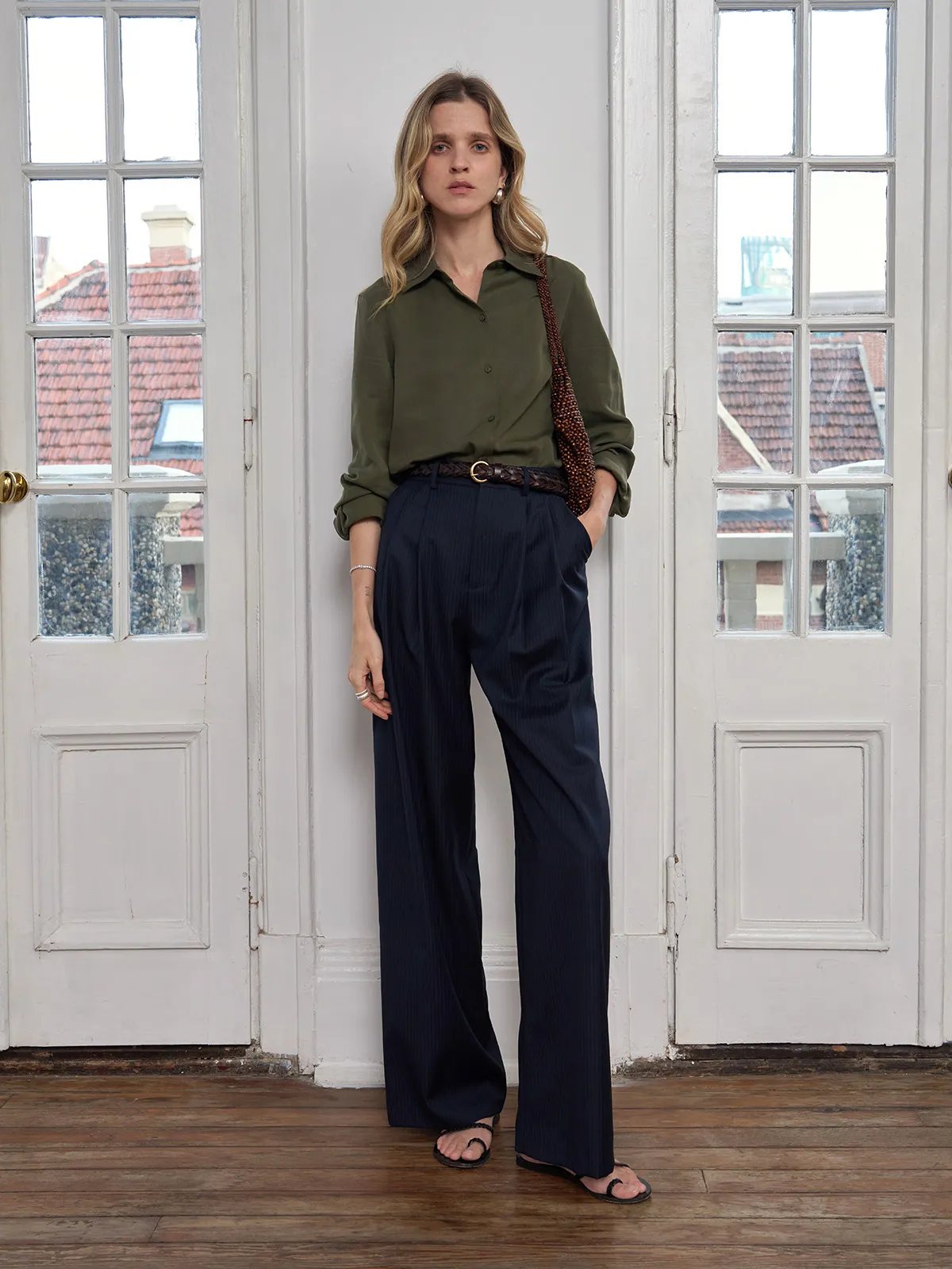 Front-facing model in olive shirt and ROGAN trousers with hands in pockets, natural light from French doors