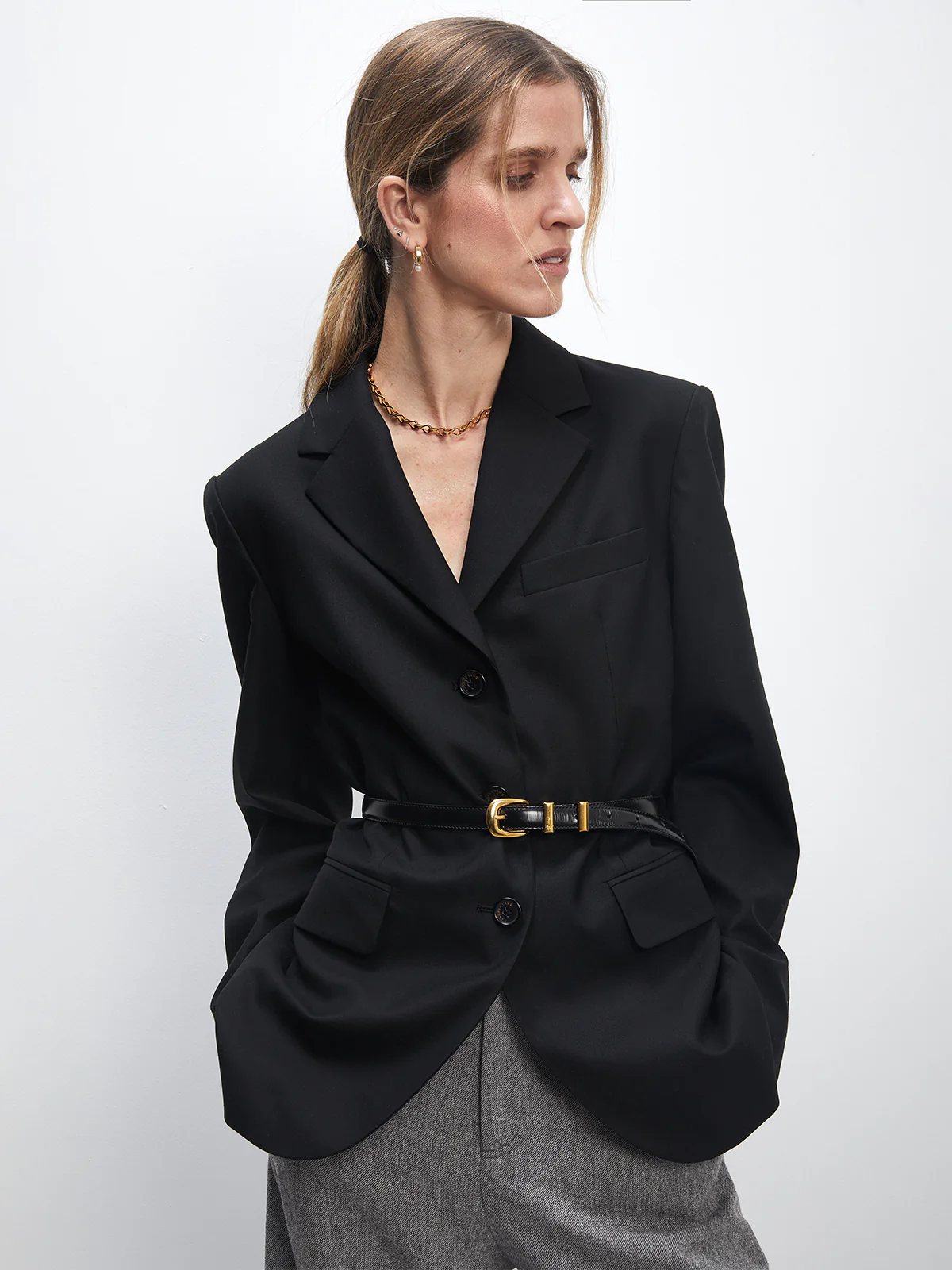 Side view of the Black Wool Acetate Cuban-Collar Blazer with a buckle belt, trousers, and black flats.