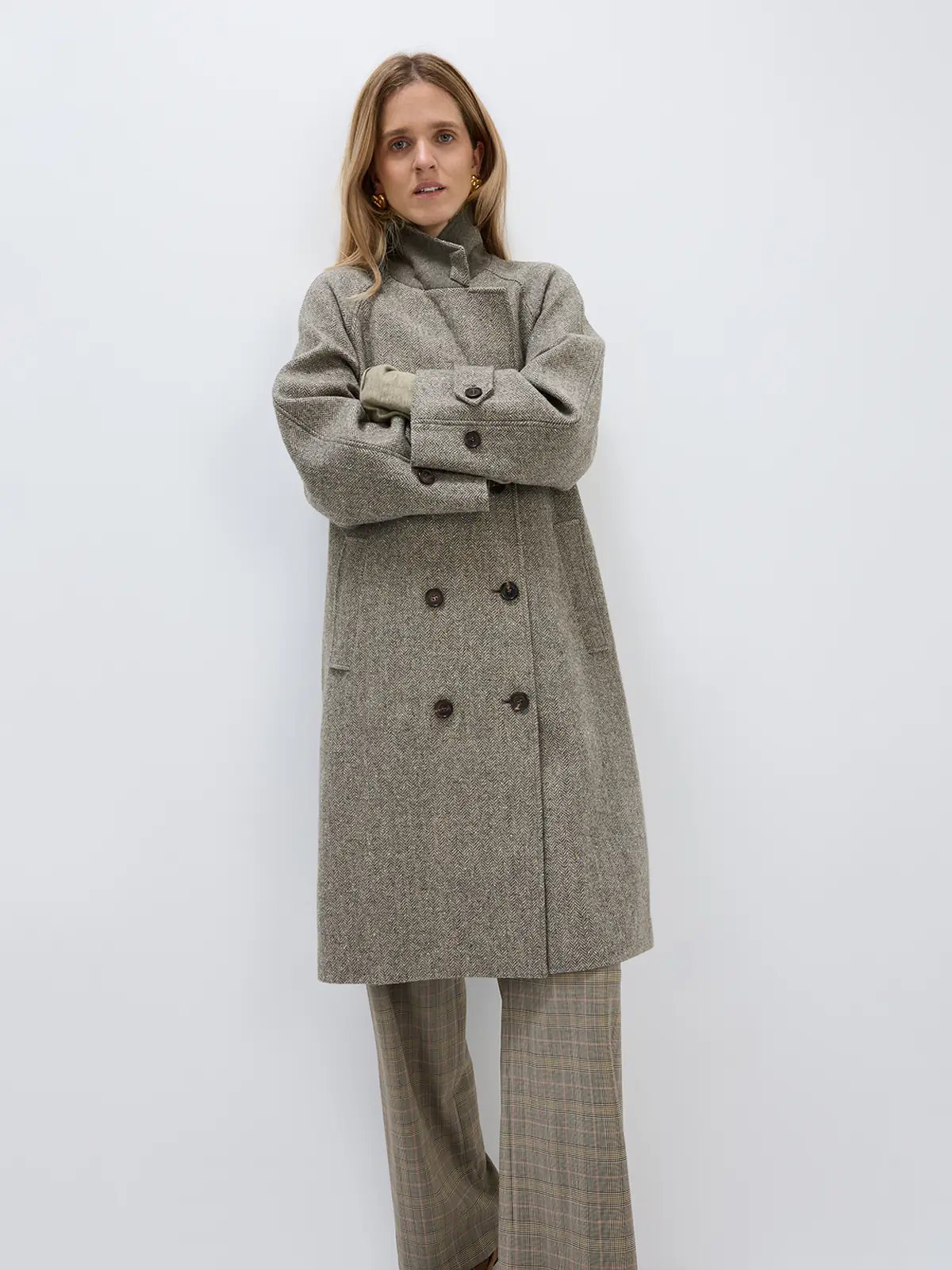 Front view of a brown herringbone double-breasted coat worn open over a shirt and jeans, hands in pockets.