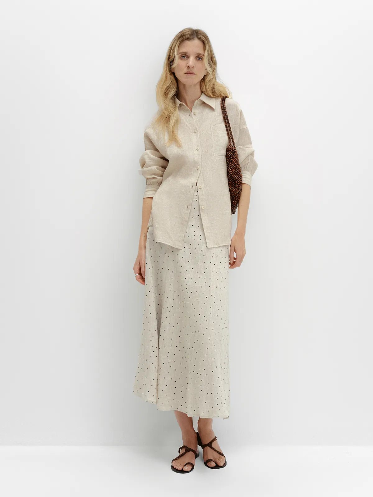 andreatang DOTTIE linen polka dot skirt styled with oat-colored button-up shirt and brown beaded bag, full-body front view