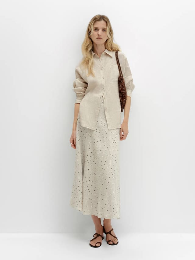 andreatang DOTTIE linen polka dot skirt styled with oat-colored button-up shirt and brown beaded bag, full-body front view