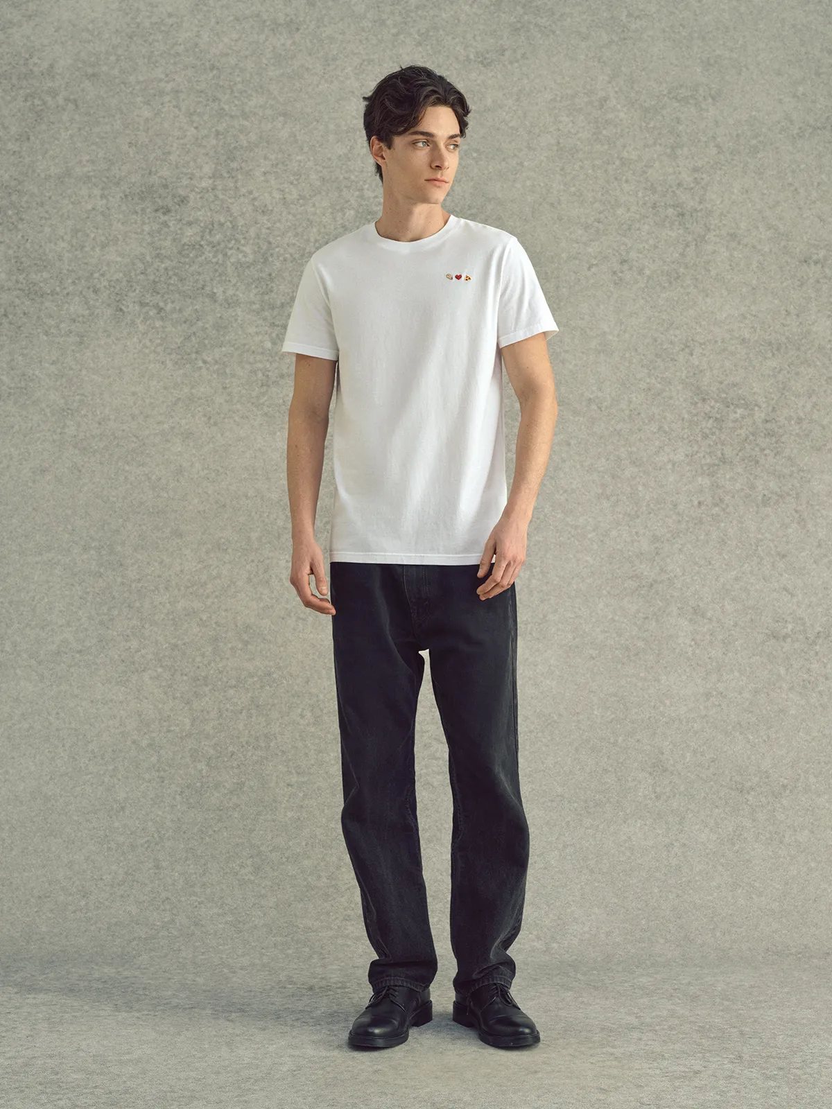 Man modeling white embroidered Lover's T-Shirt with black straight-leg jeans and leather shoes