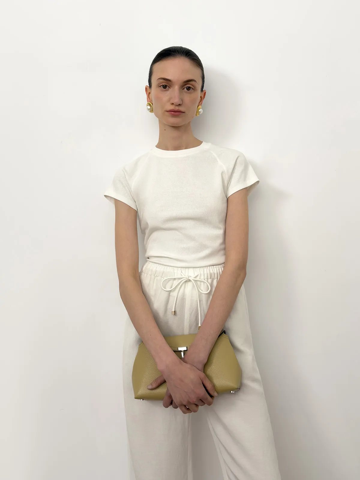 andreatang LUCA white fitted t-shirt with white drawstring pants, front-facing pose holding olive clutch