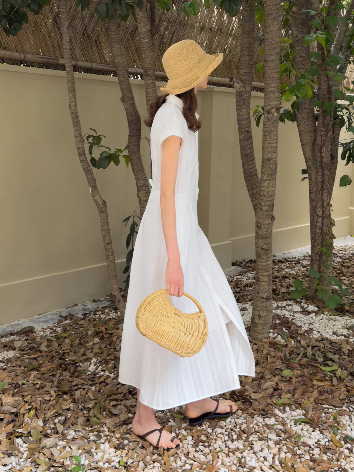 Back view of woman walking in white shirt dress with straw hat and raffia bag