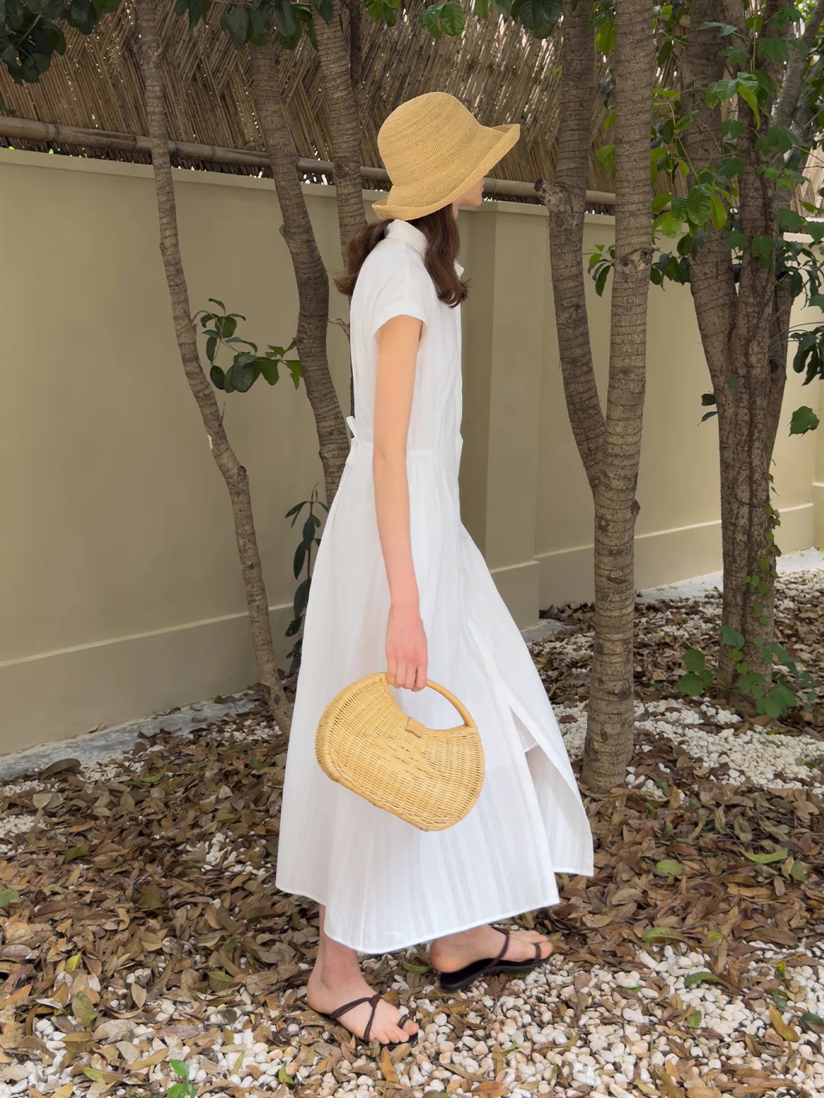 Back view of woman walking in white shirt dress with straw hat and raffia bag