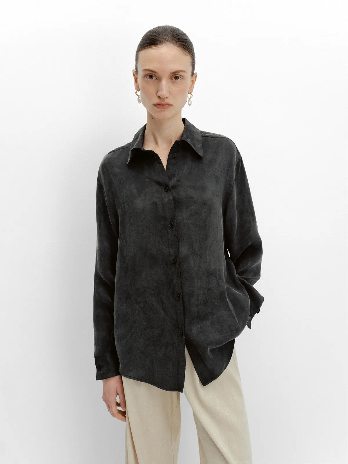 Model in black NOBU Shirt with beige wide-leg pants and pearl drop earrings