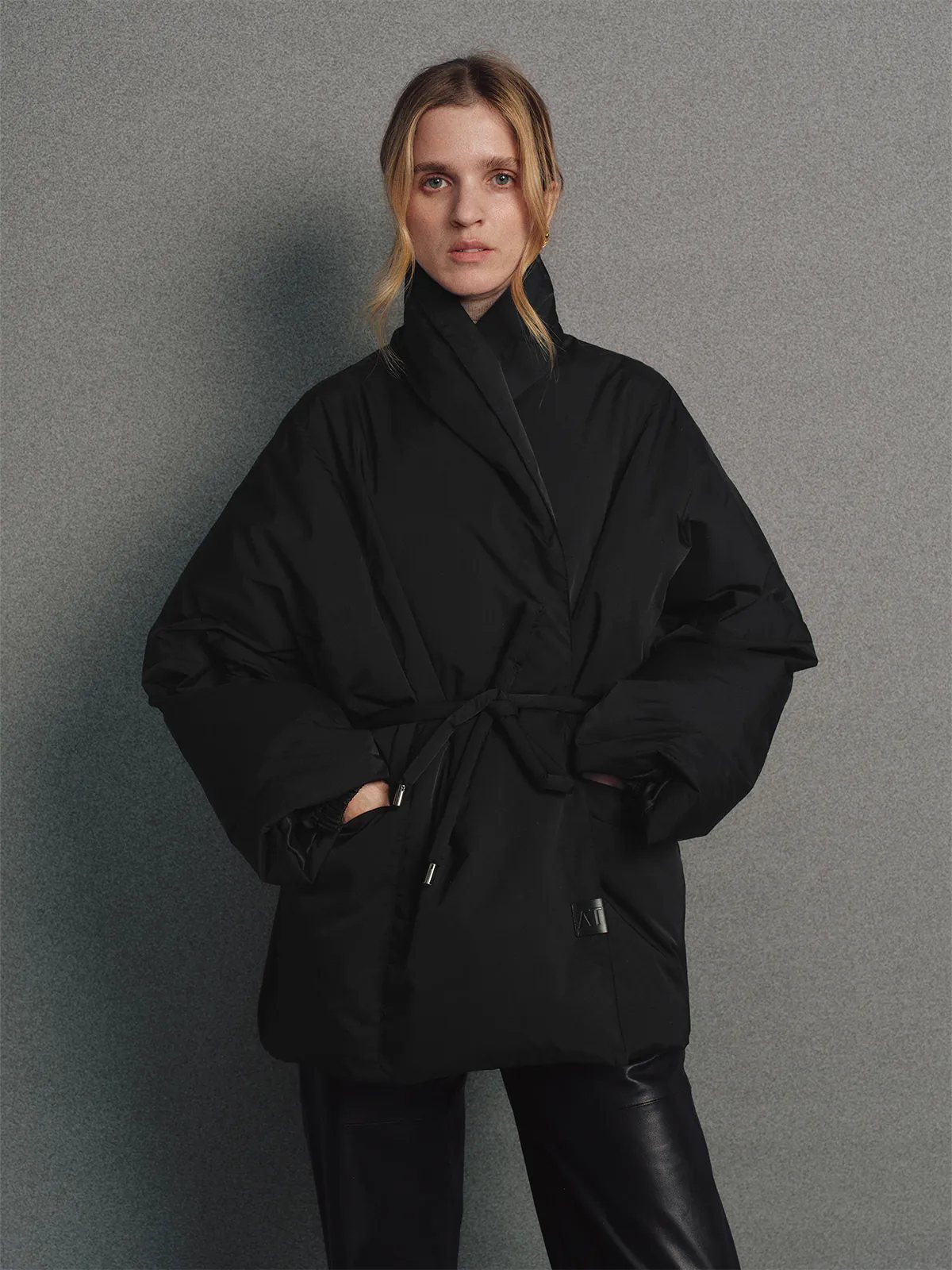 Front view of the Black OPHELIA relaxed wrap-style down coat worn over a black turtleneck and skirt, hands at sides.