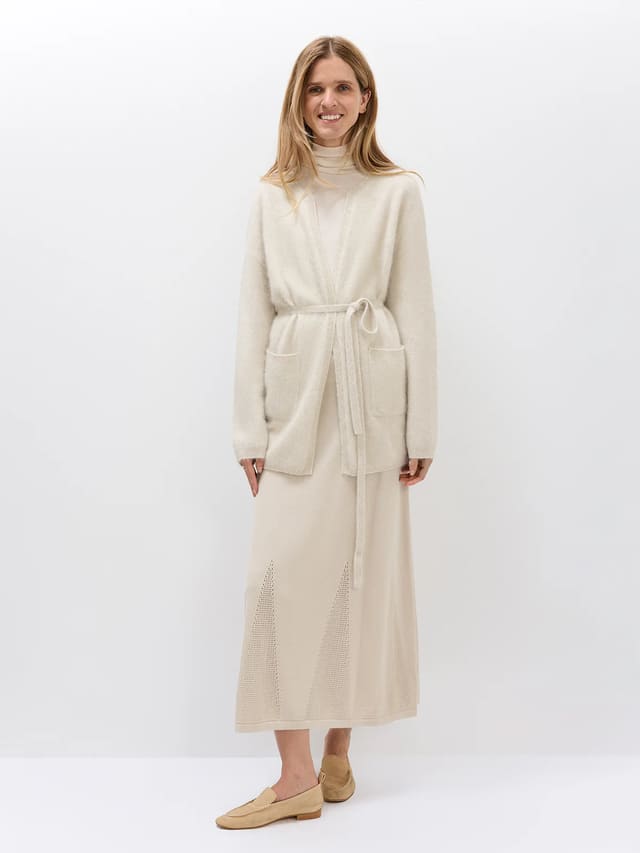 Model wearing an Oatmeal belted cardigan with front pockets and a tie waist over a matching turtleneck.