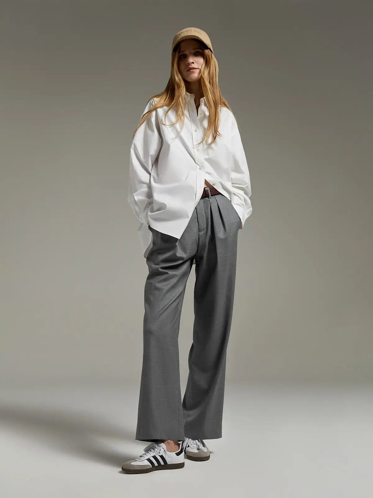 Model wearing Grey classic wool wide-leg trousers with pleats, oversized shirt, cap, and sneakers.