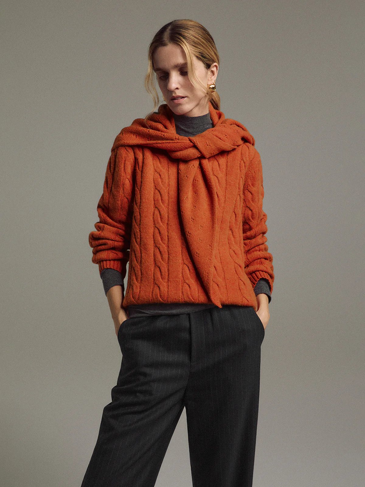 Model wears the orange yak wool triangle scarf draped over shoulders with a cable-knit sweater.
