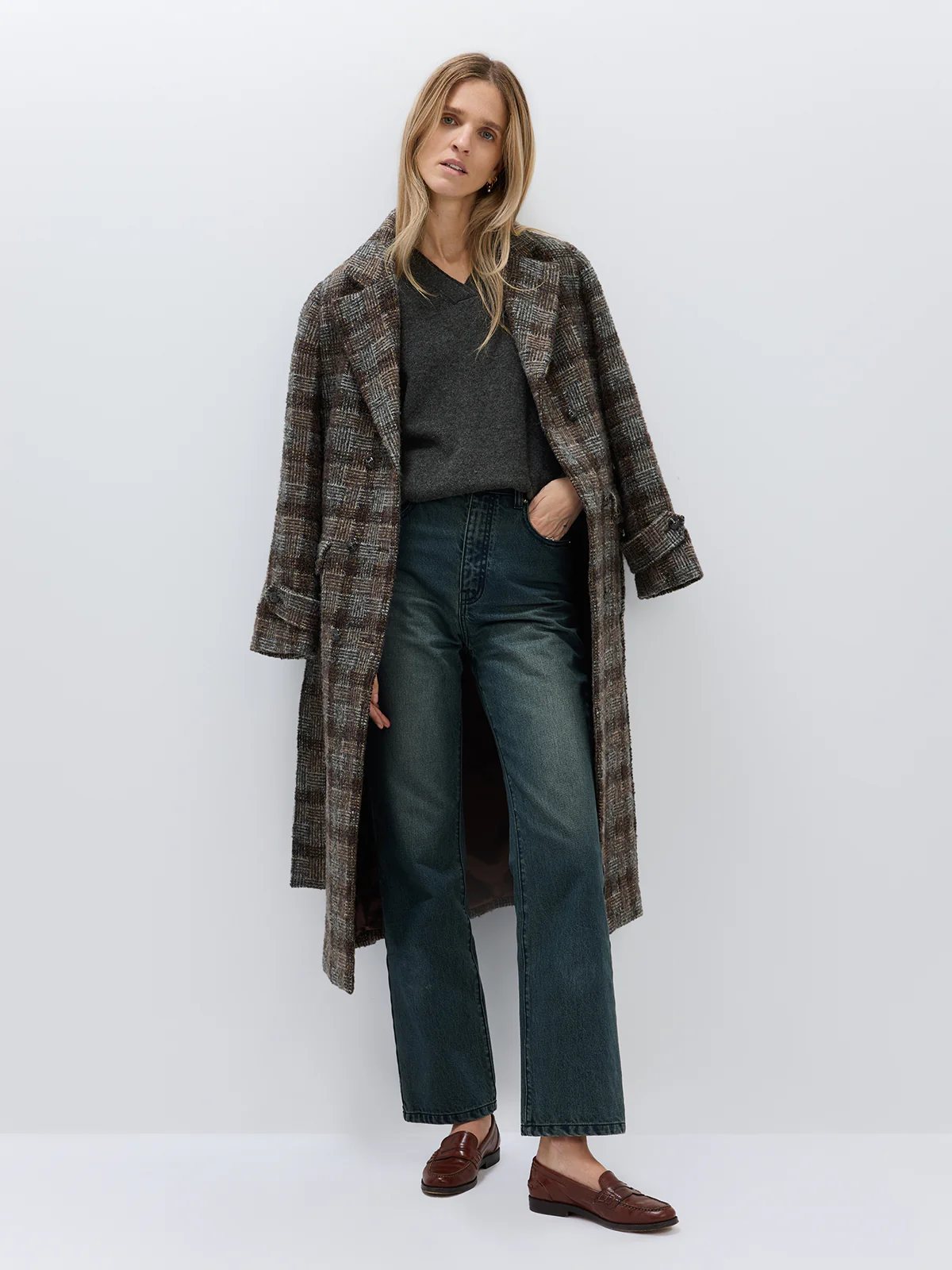 Model in Dark Brown wool alpaca tweed check coat worn open over a dark V-neck sweater and wide-leg jeans, with brown loafers.