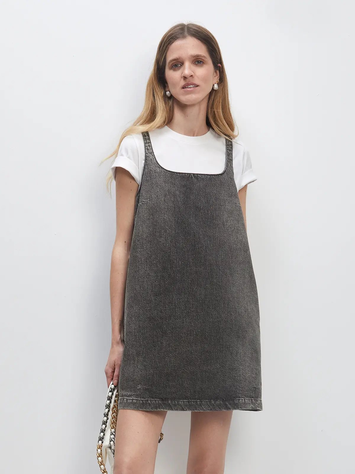 Front view of a Dark Grey retro washed A-line denim dress worn over a T-shirt with a chain-strap bag.
