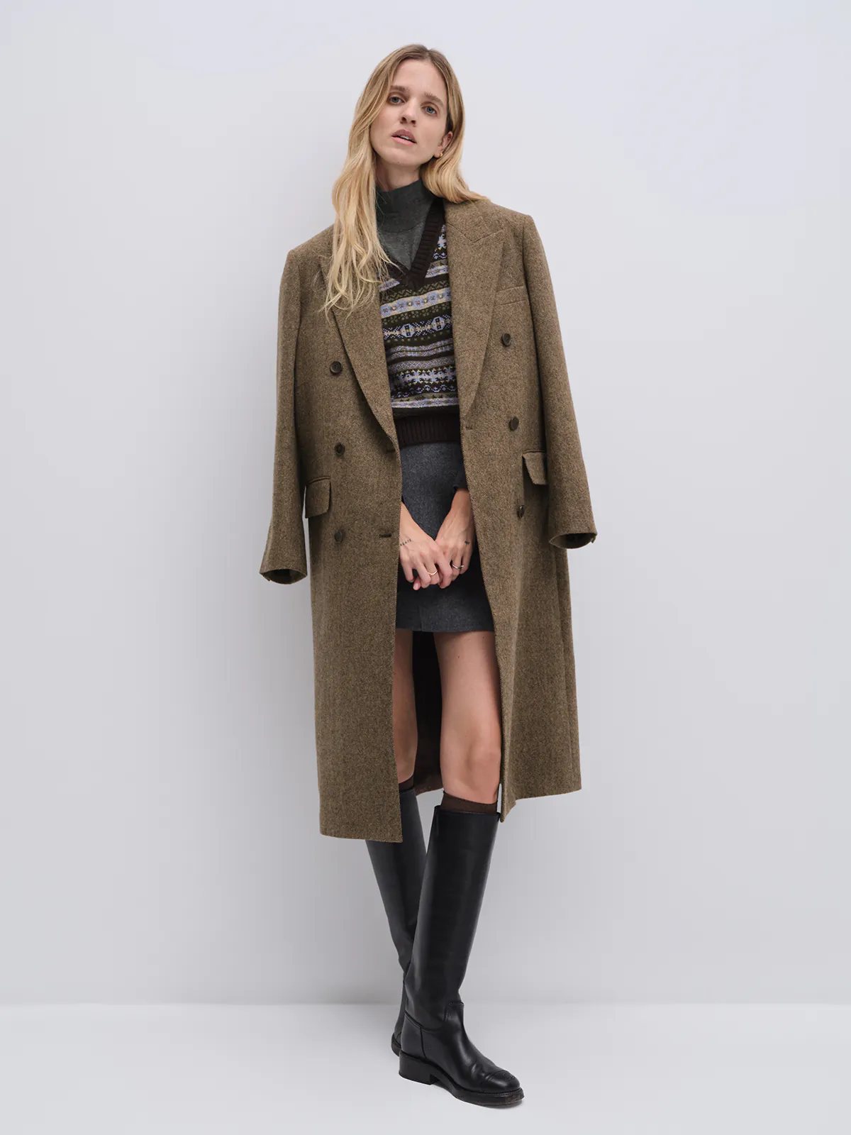 Model in a brown wool and alpaca tweed long coat, side view with hands in pockets.