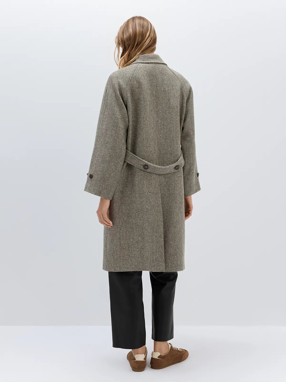 Back view of a brown herringbone double-breasted coat featuring a waist belt and buttoned cuffs, worn over trousers.