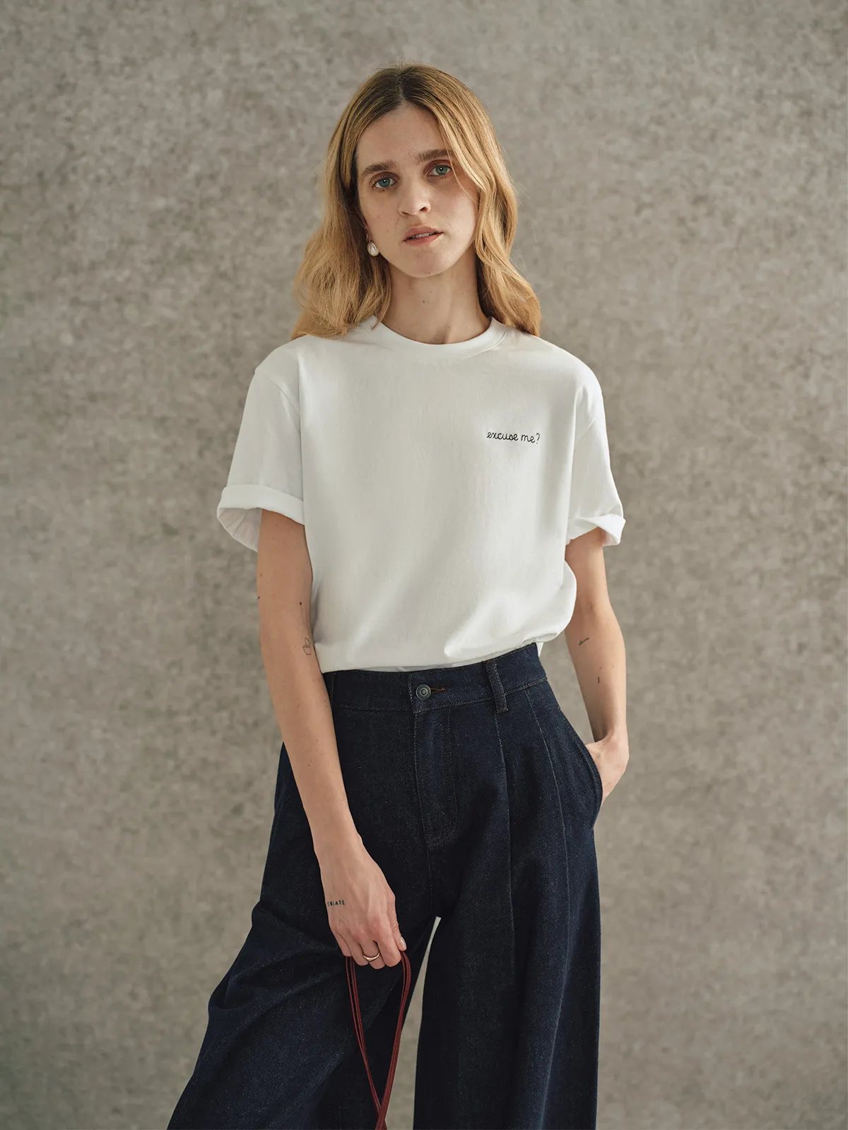 Model in white relaxed t-shirt with cuffed sleeves, navy wide-leg trousers, and red strap bag