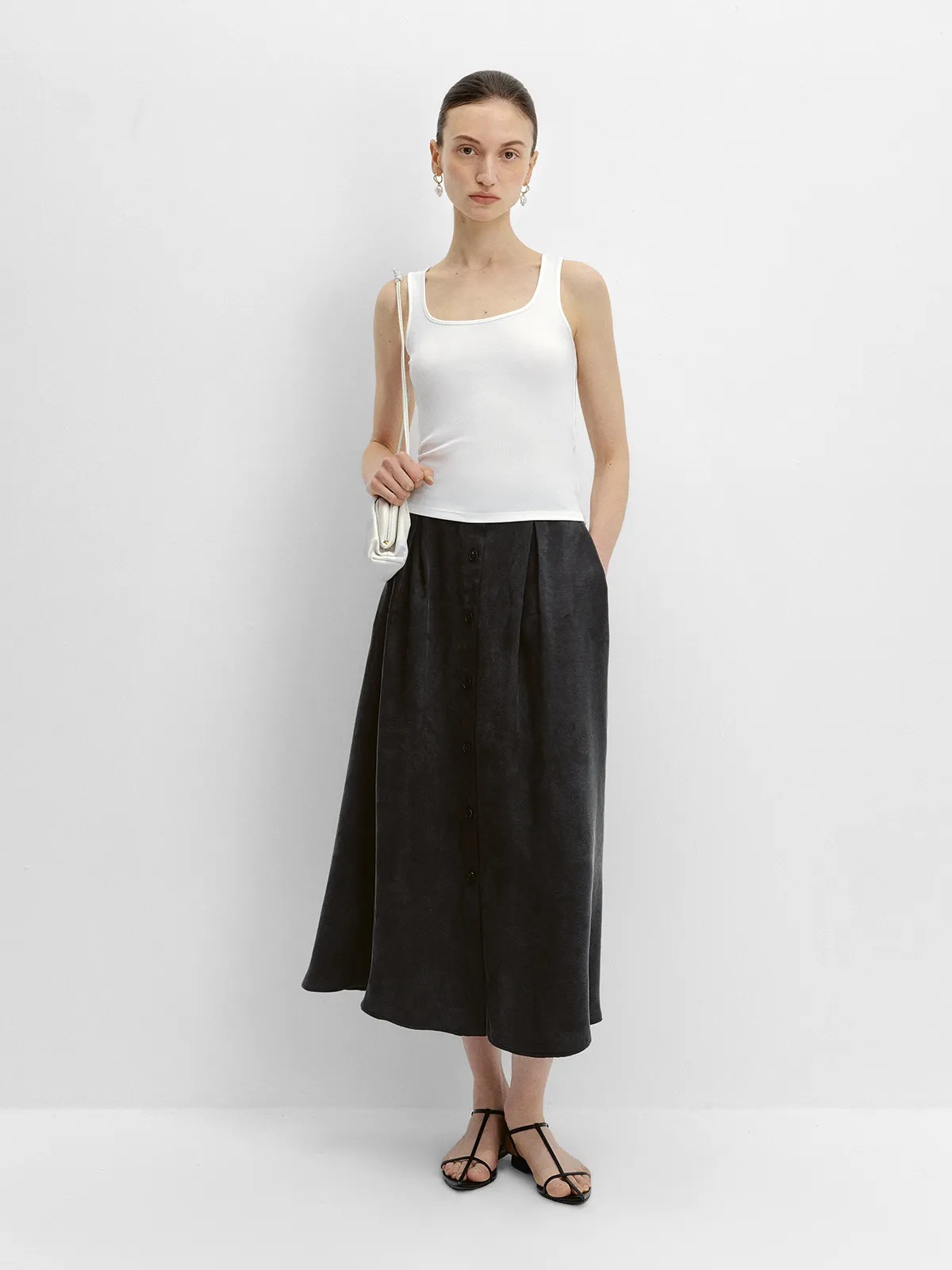 Front view of black NOBU Midi Skirt with white tank top, silver earrings, and mini shoulder bag