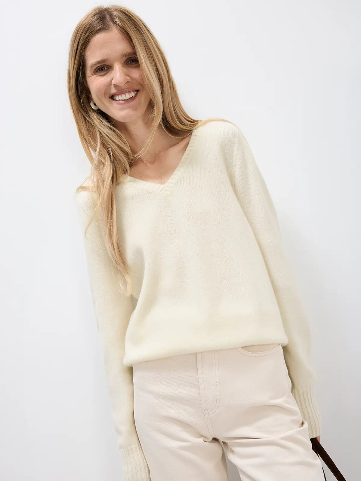 Side view of a model in a Merino Wool V-Neck Jumper paired with light trousers and holding a bag.
