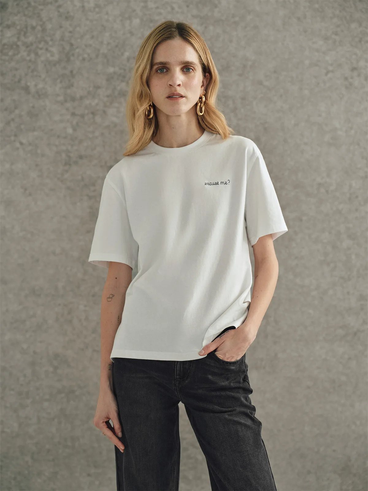 Front view of woman wearing Andreatang white relaxed t-shirt with gold hoop earrings and black jeans