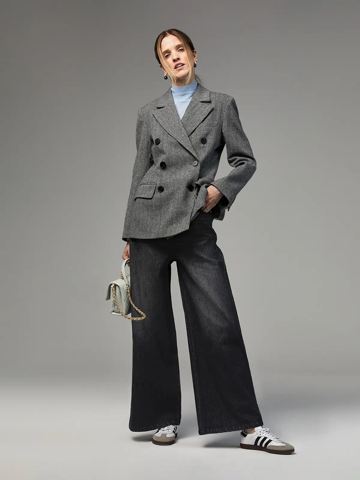 Model in Dark Grey wide-leg jeans layered under a grey double-breasted blazer, light turtleneck, and sneakers.