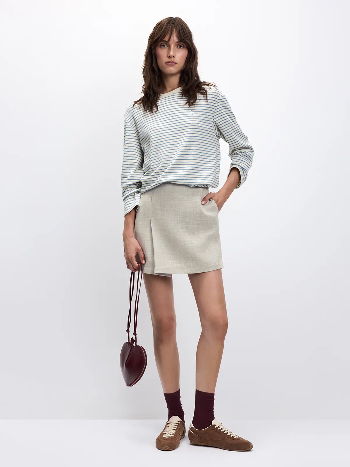 Model standing wearing a Blue/White horizontally striped long-sleeve t-shirt tucked into a light-colored mini skirt.