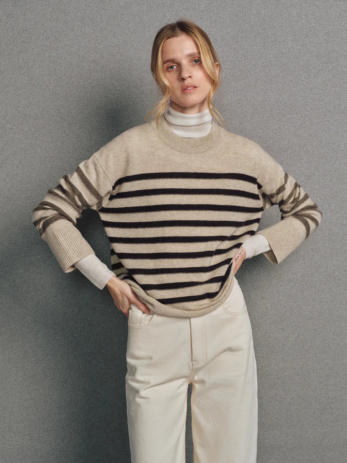 Model wearing a Light Brown contrast stripe cashmere wool jumper, side view with arms crossed.