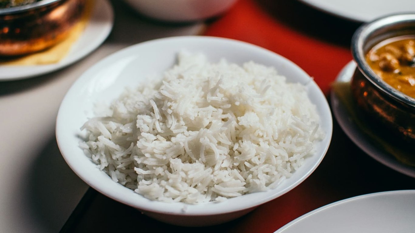 White rice in a white bowl on a table, with dishes in the background.