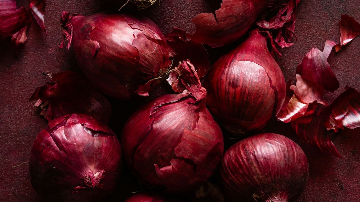 Red onions and papery skins arranged on a burgundy surface.