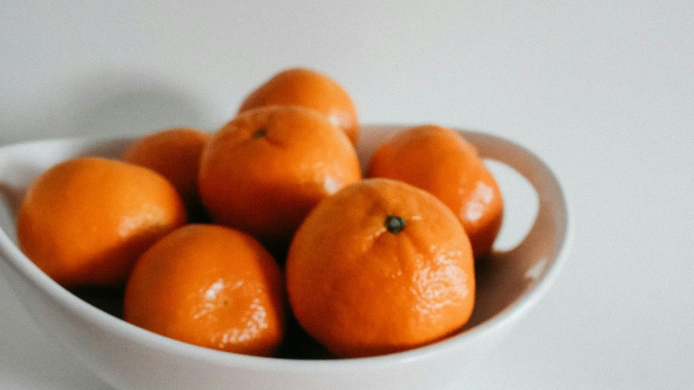 Orange citrus fruits in a white bowl on a light surface.