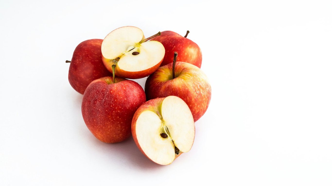 Whole and halved red apples arranged on a white surface.