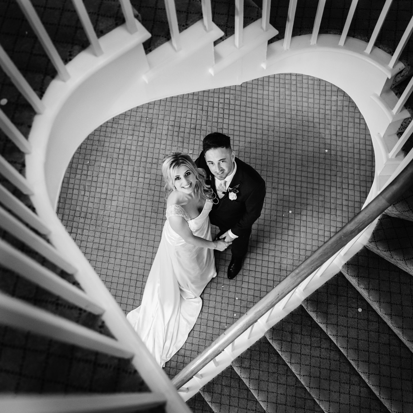 Bride and groom looking up from the foot of the spiral staircase at Fennes, photographed from above in black and white.