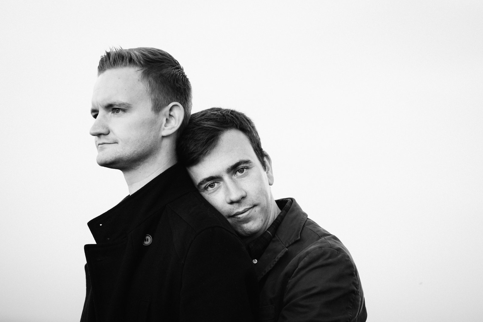 The couple standing close together against a bright white background, photographed in black and white.
