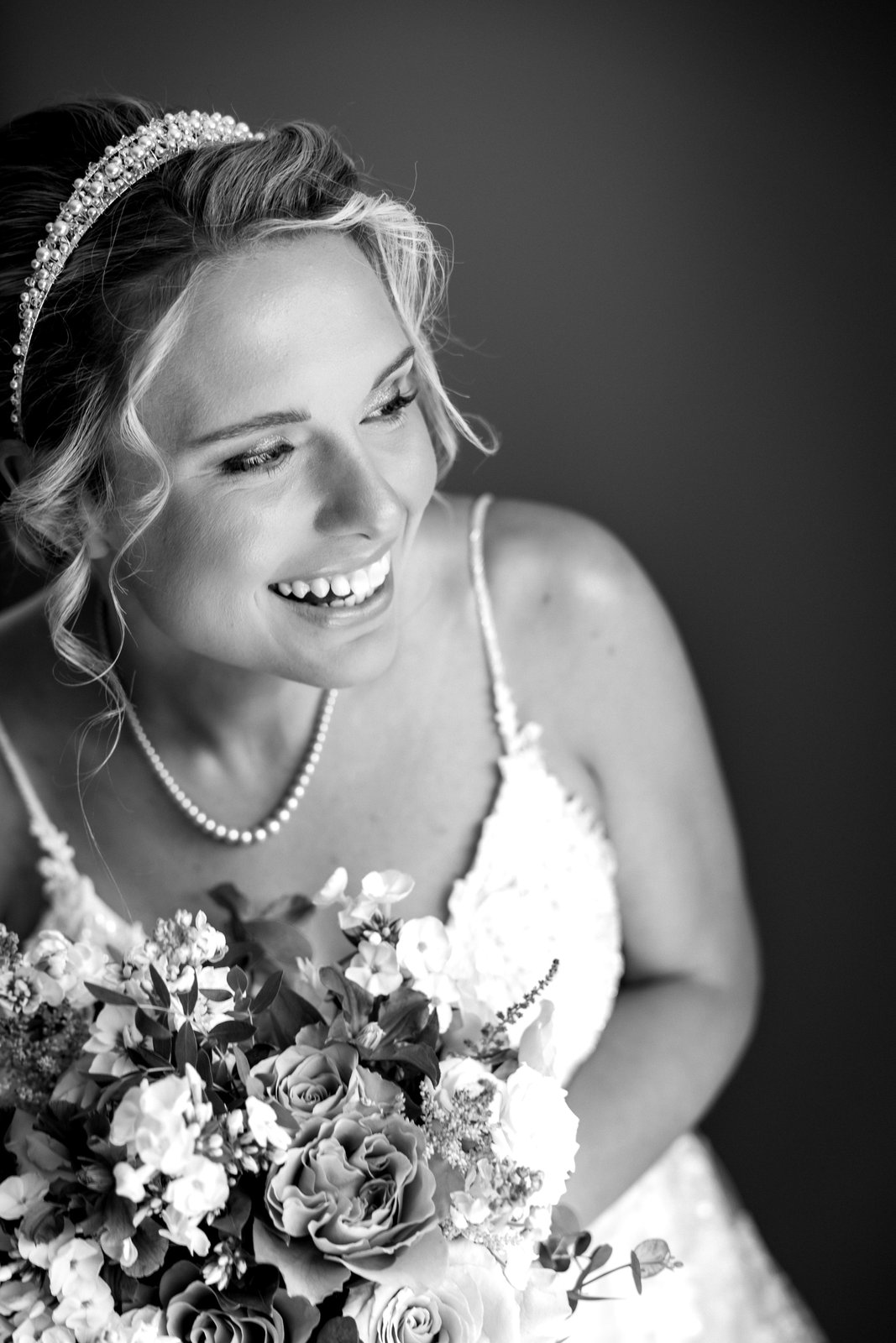 Bride laughing with her bouquet, wearing a tiara and pearls, in black and white.