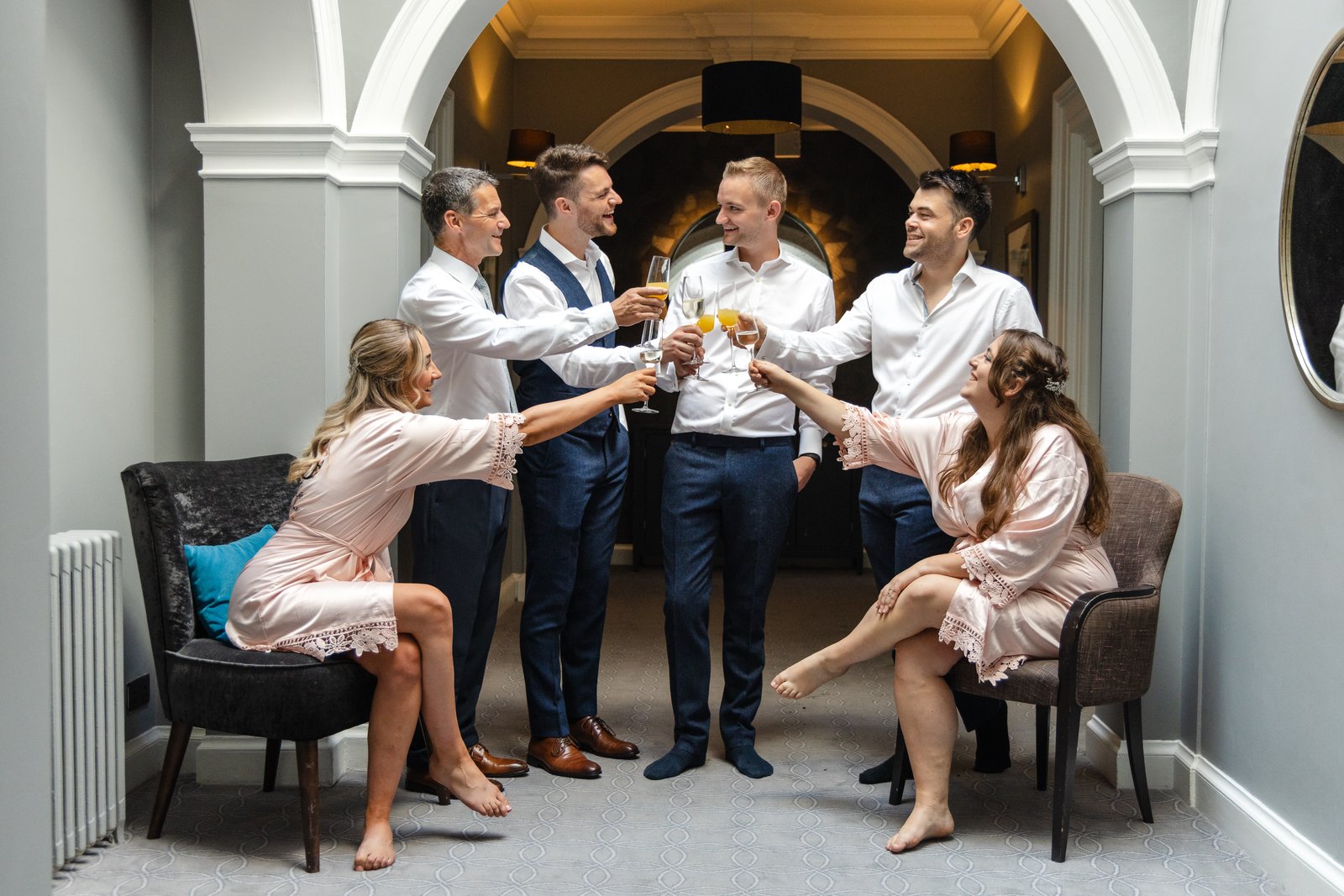 Bridesmaids in dressing gowns and groomsmen in shirtsleeves raising a toast on the morning of the wedding.