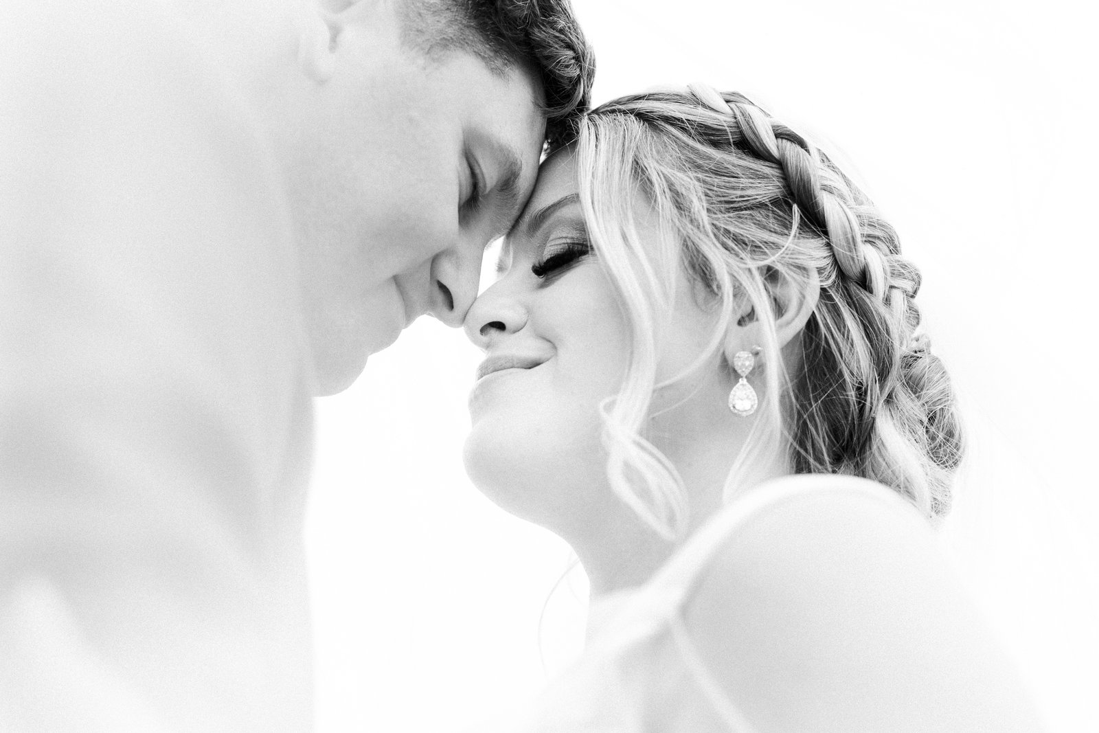 Bride and groom resting their foreheads together, photographed high-key in black and white.