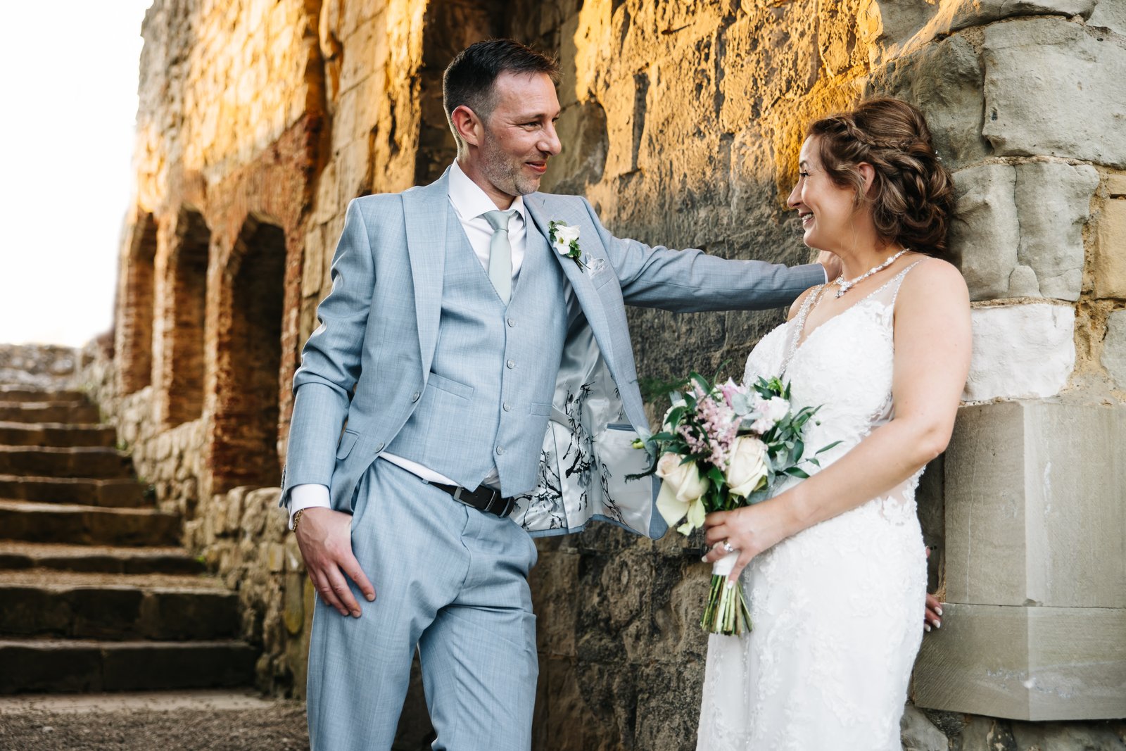 Bride and groom laughing together against the stone walls of Farnham Castle.