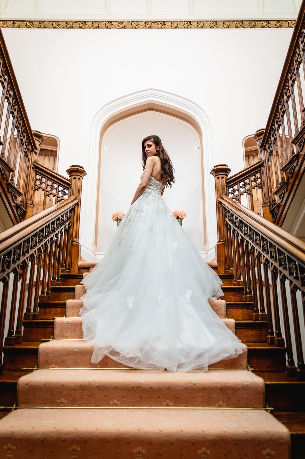 Bride pausing on the grand staircase at St Audries Park, her ballgown train spilling down the steps.