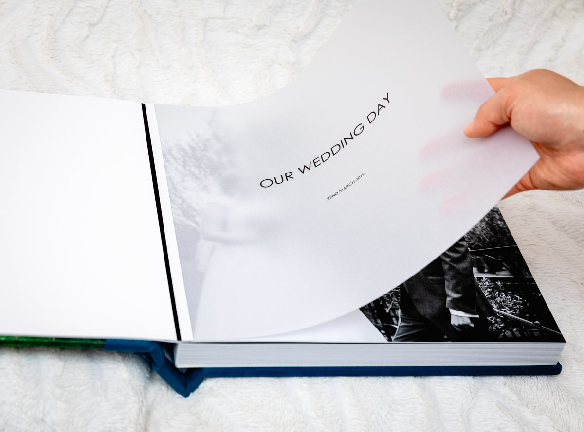Blue album open to a spread, a hand turning one of the thick lay-flat pages.