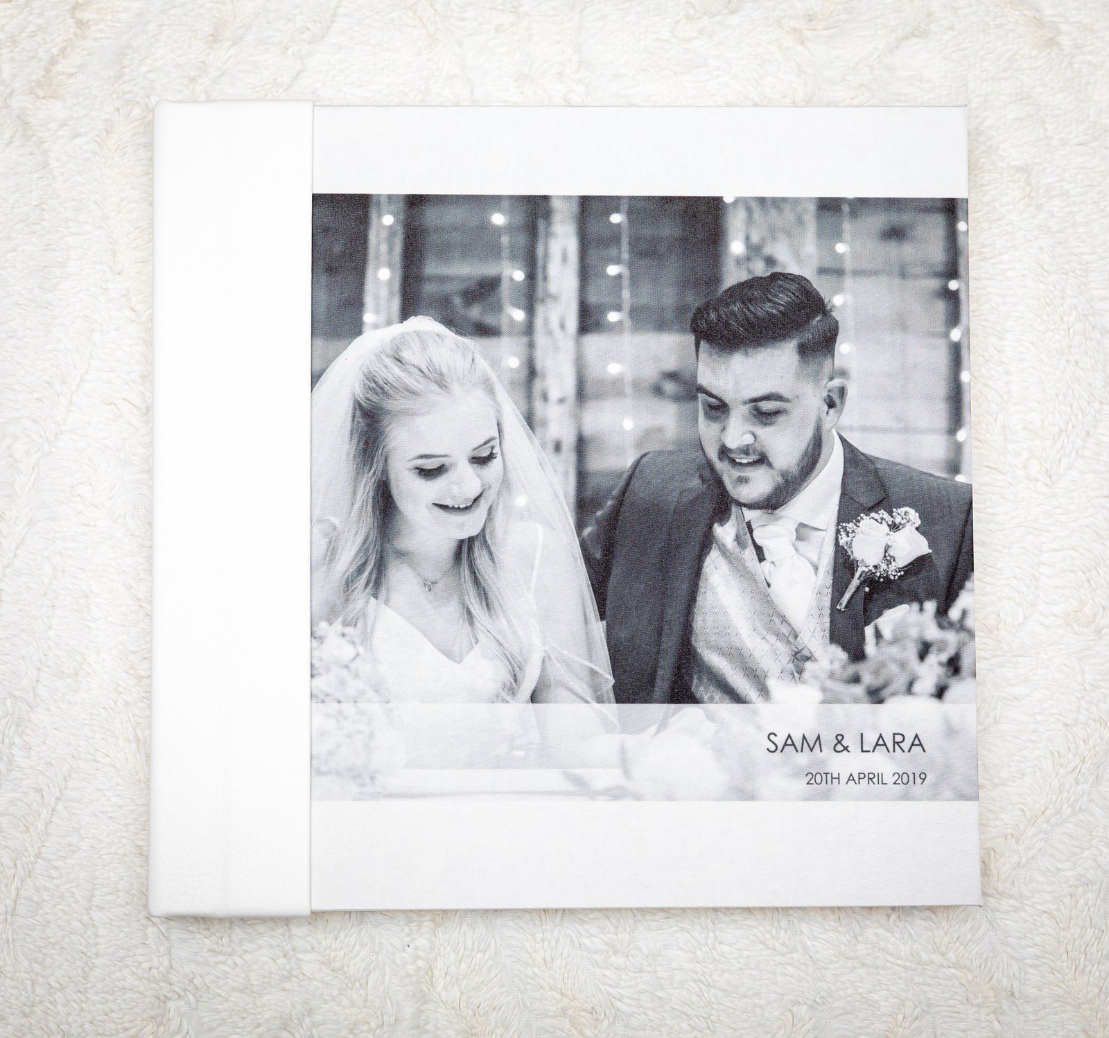 White leather album open to a black-and-white portrait of the couple printed across the page.