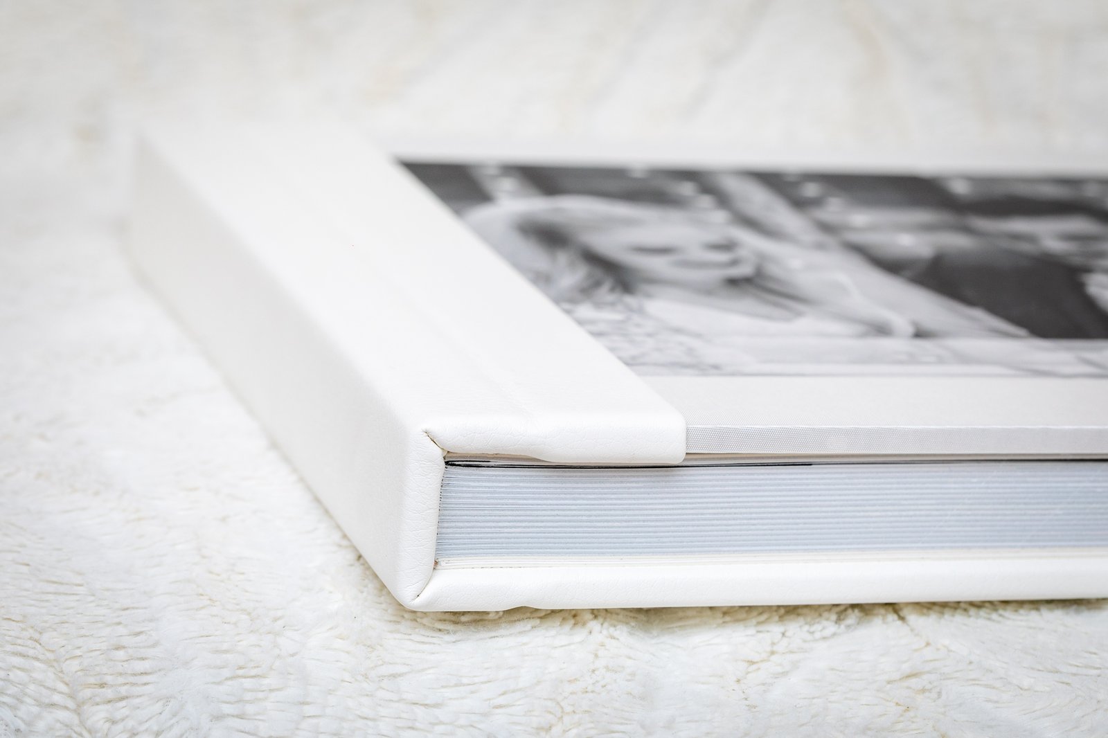 Wedding album with a white leather cover lying closed on a soft background.