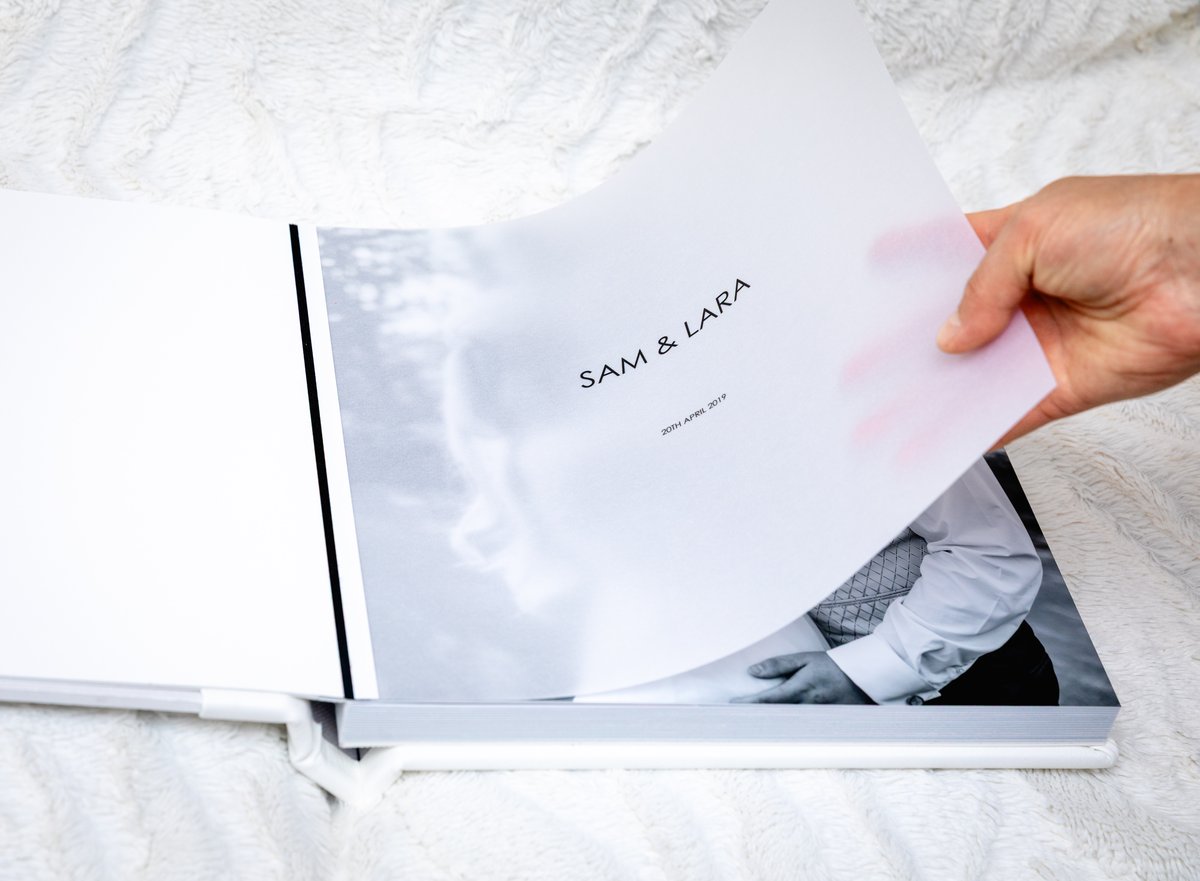 Hand turning a page inside the white leather album.