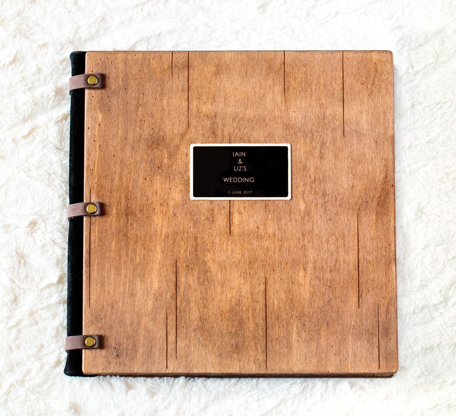 Wedding album with a rustic wooden cover, leather-strap binding and an engraved nameplate, photographed from above.