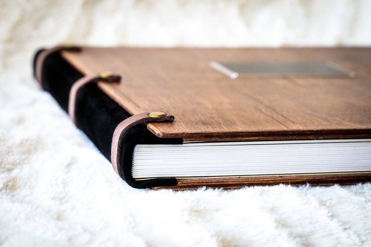 Wooden-cover album seen at an angle, showing the timber front and leather spine.