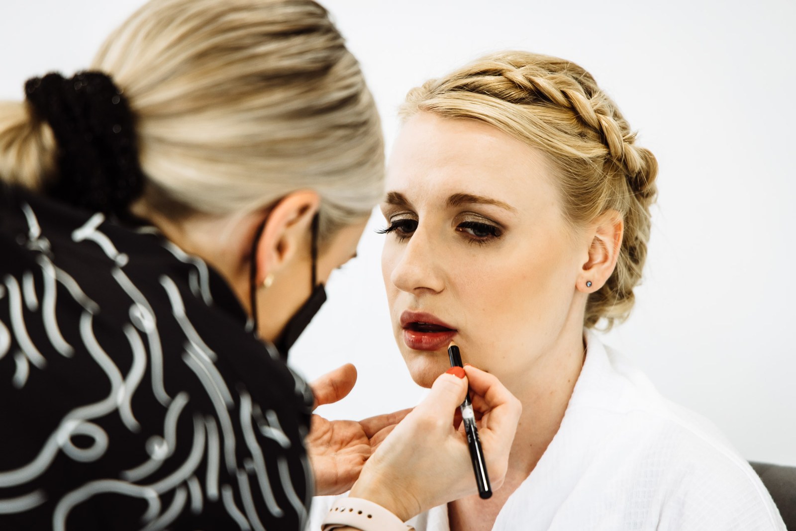 A makeup artist applying lipstick to the bride during morning preparations