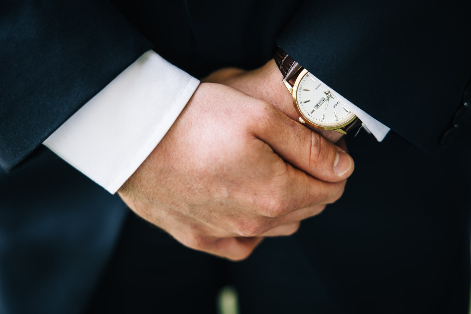 Close-up of the groom's clasped hands and gold wristwatch before the ceremony