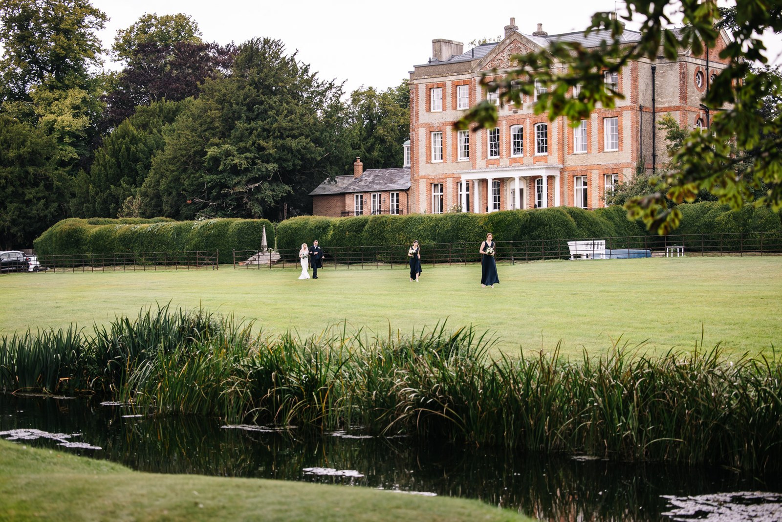 Ardington House seen across the reed-fringed pond, guests gathering on the far lawn