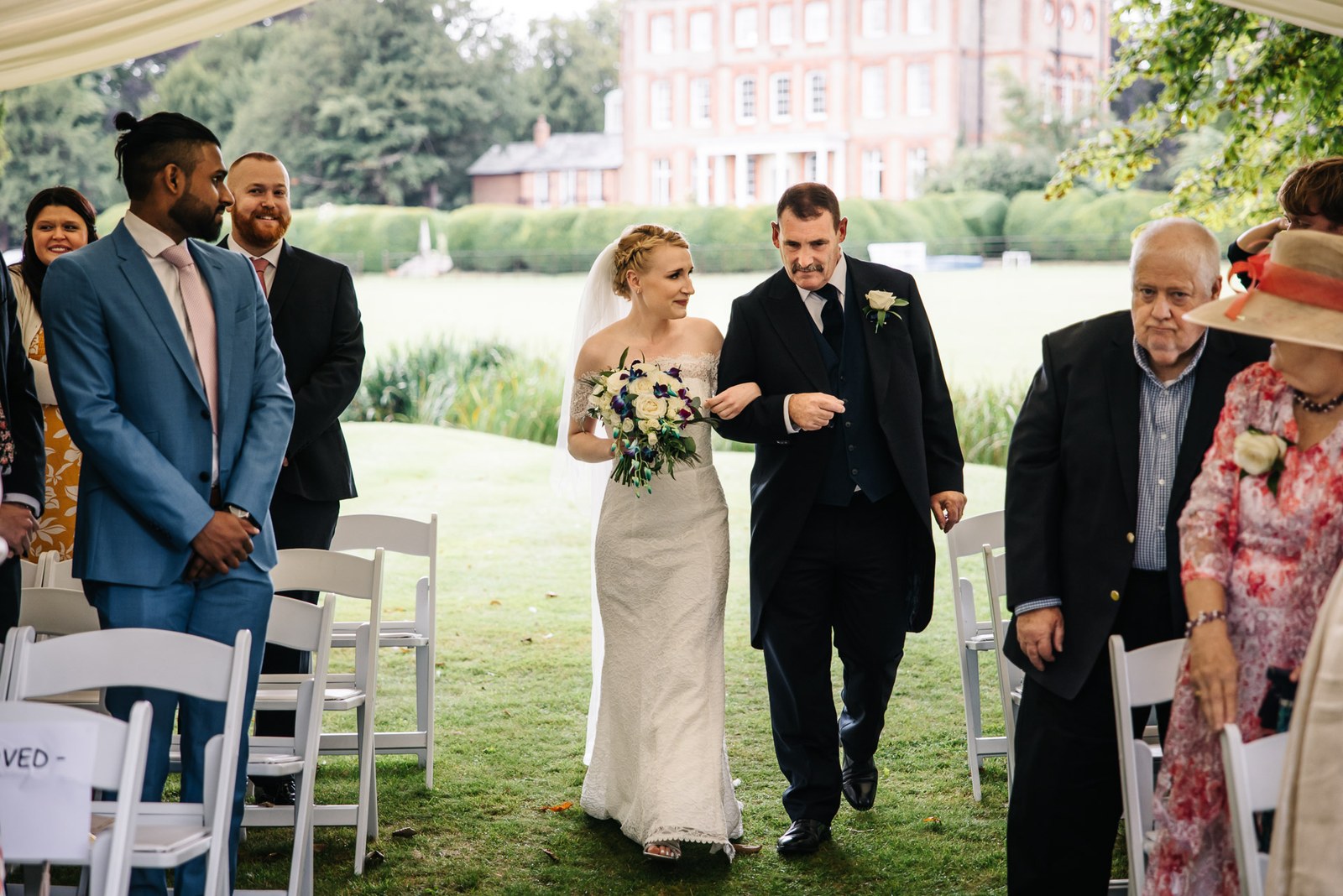The bride walking to the ceremony on her father's arm, the house behind